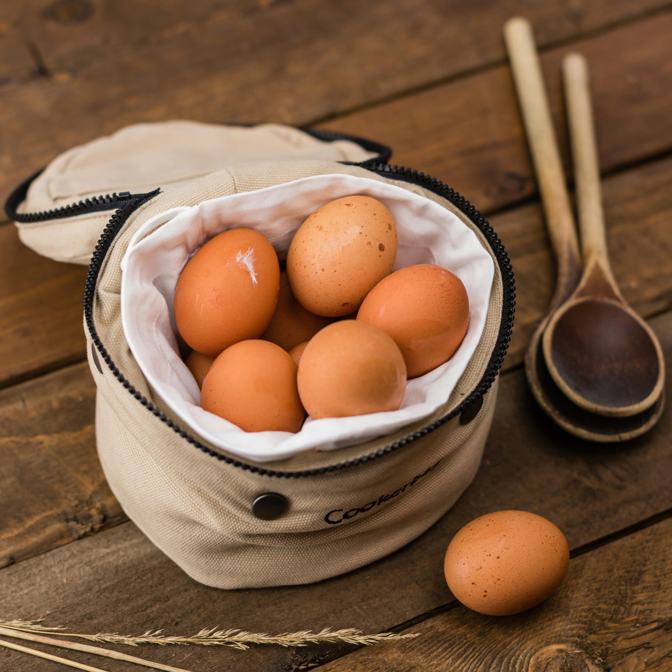 A rustic kitchen scene with fresh eggs in a bag and wooden spoons on a wooden table.