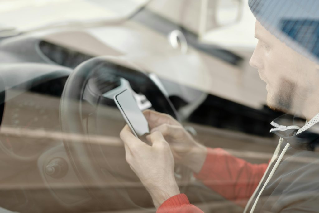 Caucasian man in red hoodie using smartphone while sitting in a car.